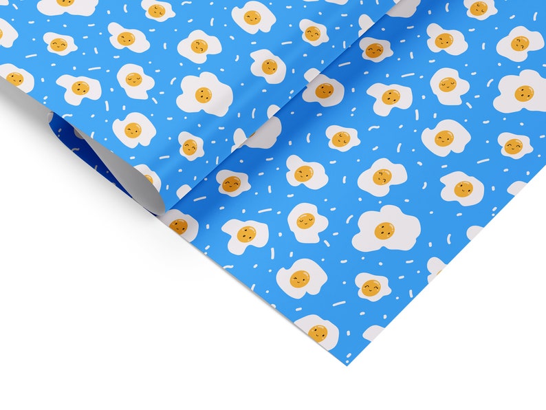 May include: A blue wrapping paper with a repeating pattern of white fried eggs with yellow yolks and smiling faces. The eggs are scattered randomly on a blue background with white dashes.