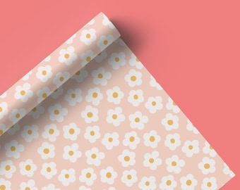 Op de afbeelding: Een rol roze cadeaupapier met een wit madeliefjespatroon. Het papier is opgerold en het uiteinde is zichtbaar.