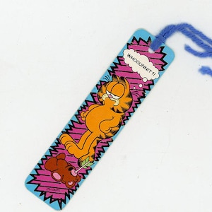 May include: A Garfield bookmark with the orange cat and a brown teddy bear. The bookmark has a blue zig-zag border with the text "WHODUNNIT?!" in a speech bubble. A blue yarn tassel is attached.