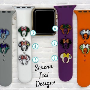 May include: Four different colored Apple Watch bands with various Mickey Mouse ear charms attached. The bands are gray, white, purple, and orange. The charms are decorated with glitter and different patterns.