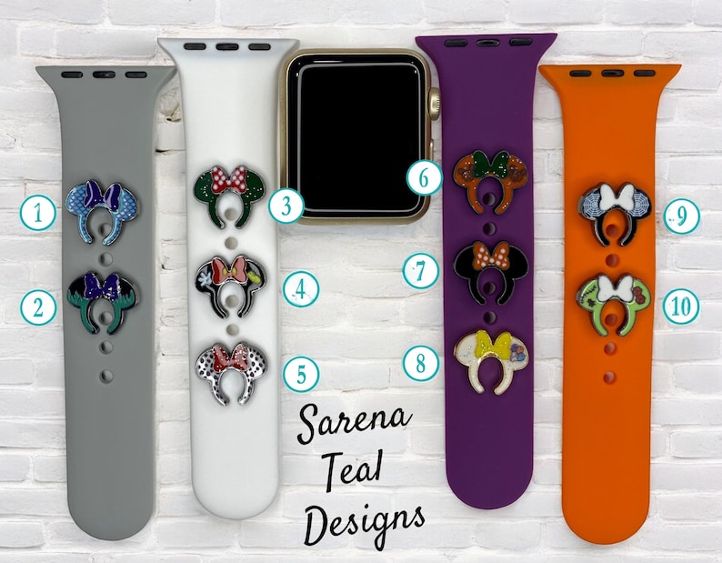 May include: Four different colored Apple Watch bands with various Mickey Mouse ear charms attached. The bands are gray, white, purple, and orange. The charms are decorated with glitter and different patterns.