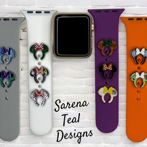 May include: Four different colored Apple Watch bands with various Disney character themed charms attached. The charms are all of Mickey Mouse's ears with different designs. The bands are gray, white, purple, and orange. The text "Sarena Teal Designs" is visible below the bands.