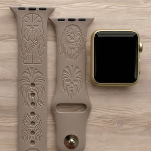 May include: A beige silicone Apple Watch band with a repeating pattern of Chewbacca's face. The band is shown with a gold Apple Watch.