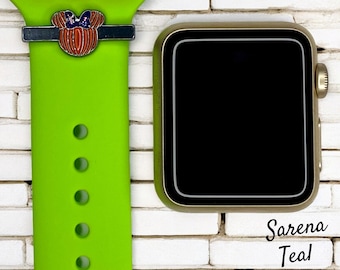 Könnte beinhalten: Ein grünes Apple Watch-Armband mit einem schwarzen und silbernen Mickey Mouse-Anhänger. Der Anhänger hat eine rote Schleife und einen orangefarbenen Kürbis. Das Armband hat fünf Löcher zum Einstellen der Passform. Das Armband ist neben einer goldenen Apple Watch abgebildet.