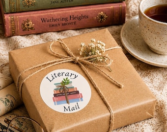 May include: A square gift box wrapped in brown paper, tied with twine and a small sprig of white flowers. A circular sticker on the box features a stack of books and the text Literary Mail. Nearby are three classic books, a teacup, and glasses.