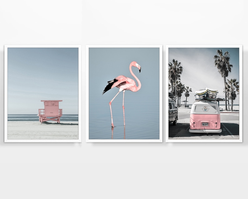 May include: Set of three framed prints featuring beach scenes. One shows a pink lifeguard stand on a sandy beach, another a pink flamingo in water, and the third a pink van with surfboards, palm trees in the background.
