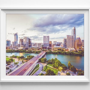 K&ouml;nnte beinhalten: Ein Panoramablick auf die Skyline von Austin, Texas, mit einer Br&uuml;cke im Vordergrund. Die Stadt ist voller Wolkenkratzer und moderner Geb&auml;ude. Der Himmel ist eine Mischung aus Blau und Grau mit Wolken.