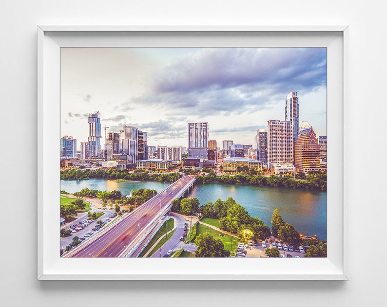 K&ouml;nnte beinhalten: Ein Panoramablick auf die Skyline von Austin, Texas, mit einer Br&uuml;cke im Vordergrund. Die Stadt ist voller Wolkenkratzer und moderner Geb&auml;ude. Der Himmel ist eine Mischung aus Blau und Grau mit Wolken.