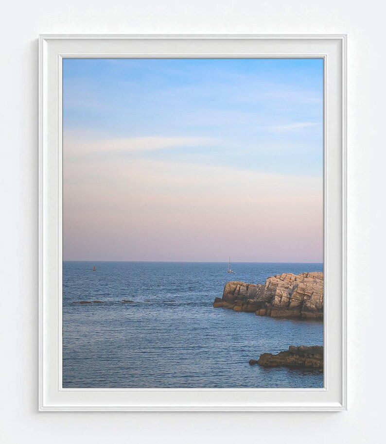 Pu&ograve; includere: Una fotografia incorniciata di un paesaggio marino con un cielo blu e una costa rocciosa. L'acqua &egrave; di un blu profondo e il cielo &egrave; di un azzurro chiaro con un tocco di rosa. Ci sono due piccole barche in lontananza.