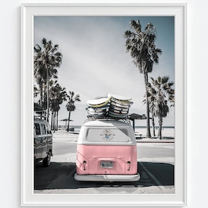 May include: A framed print featuring a pink and white vintage van parked on a beach, topped with surfboards. Palm trees line the beach and the van has a California license plate. The sky is a pale blue.
