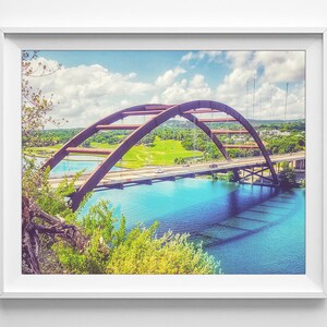 K&ouml;nnte beinhalten: Eine rote Stahlbr&uuml;cke w&ouml;lbt sich &uuml;ber ein blaues Gew&auml;sser. Die Br&uuml;cke hat eine Stra&szlig;e und Autos fahren dar&uuml;ber. Das Wasser ist von gr&uuml;nen B&auml;umen und Gras umgeben.