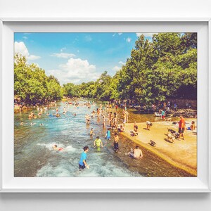 K&ouml;nnte beinhalten: Ein sonniger Tag an einem Fluss, auf dem Menschen schwimmen und im Wasser spielen. Der Fluss ist von B&auml;umen umgeben und auf der rechten Seite des Bildes befindet sich ein Sandstrand.