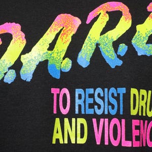 May include: Black fabric with the D.A.R.E. logo in neon colors. The text "TO RESIST DRUGS AND VIOLENCE" is below the logo, also in neon colors. The design has a retro, 80s or 90s aesthetic.