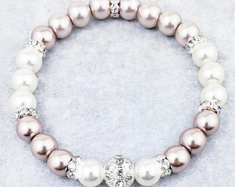 May include: A white and blush pink pearl bracelet with a rhinestone accent. The bracelet has a large, sparkly rhinestone ball charm in the centre.