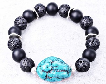 Pode incluir: Um bracelete de contas de lava negra e ônix com um ponto focal de pedra turquesa. O bracelete tem contas espaçadoras prateadas.