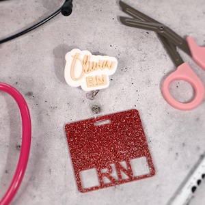 Custom acrylic badge reel engraved with name Olivia and title RN. Personalized retractable ID holder for nurses, CNAs, and healthcare professionals. Shown in white base with gold text, featuring 360° alligator clip and 25-inch retractable cord. Durable, lightweight, and handcrafted acrylic design perfect for hospital staff, clinics, and nurse week gifts. Stylish and functional nurse badge reel made in the USA.