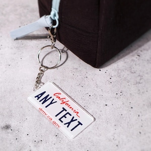 Custom 50-state license plate keychain featuring realistic state graphics and customizable text. Made from durable acrylic with metal chain — perfect for car keys, backpacks, or luggage tags. A creative, unique gift for drivers, car enthusiasts, and new car owners. Collect your favorite states or personalize for each road trip memory. Great for bulk gifting and car merch.