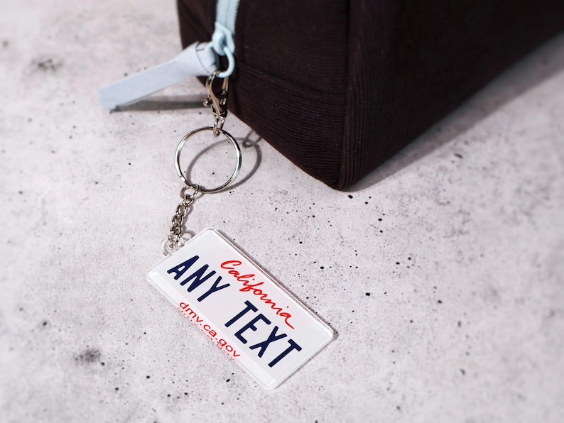 Custom 50-state license plate keychain featuring realistic state graphics and customizable text. Made from durable acrylic with metal chain — perfect for car keys, backpacks, or luggage tags. A creative, unique gift for drivers, car enthusiasts, and new car owners. Collect your favorite states or personalize for each road trip memory. Great for bulk gifting and car merch.