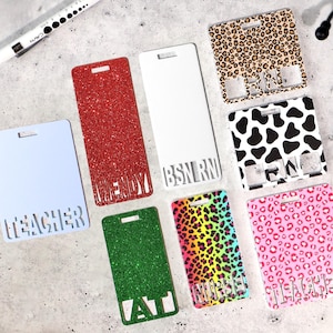 Può includere: Una collezione di porta badge rettangolari in vari colori e fantasie. Alcuni sono a tinta unita, come glitter rosso, glitter verde e azzurro. Altri presentano stampe animalier, tra cui motivi leopardati e mucca. Ritagli di testo identificano ruoli come "TEACHER" e "NURSE".
