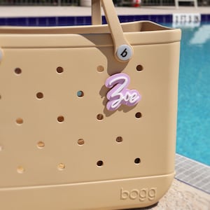 Custom acrylic name tag for Bogg Bag lavender and white, perfect for adding a personalized touch. Ideal Bogg Bag accessory and gift idea for birthdays, teachers, or bridesmaids. Fits Original and Baby Bogg Bags. Great for pink Bogg Bags, Crocs-style bags, gym bags, or diaper bags. Use as a name plate, initial charm, or cute Bogg Bag name. Personalize with your name or word of choice. Stylish, practical, and fun way to customize your Bogg Bag