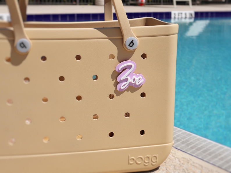 Custom acrylic name tag for Bogg Bag lavender and white, perfect for adding a personalized touch. Ideal Bogg Bag accessory and gift idea for birthdays, teachers, or bridesmaids. Fits Original and Baby Bogg Bags. Great for pink Bogg Bags, Crocs-style bags, gym bags, or diaper bags. Use as a name plate, initial charm, or cute Bogg Bag name. Personalize with your name or word of choice. Stylish, practical, and fun way to customize your Bogg Bag