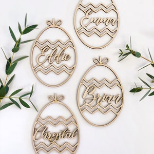 May include: Four wooden Easter egg ornaments with chevron patterns and names "Emma", "Addie", "Brian", and "Crystal" written in cursive.