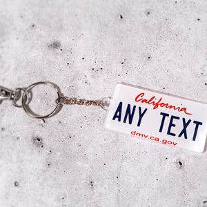Custom plate keychain available in 50 state styles. Add your own name, initials, or phrase to create a one-of-a-kind keyring. Acrylic material with glossy finish gives a realistic license look. Great for car lovers, new drivers, or travel enthusiasts who want to show off their favorite state. A stylish, personalized, and functional car accessory gift.