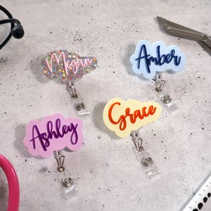 Group of personalized acrylic badge reels in mixed pastel and glitter colors. Custom name tag reels for nurses, teachers, and medical professionals. Retractable ID holders with alligator clips, handcrafted in the USA. Perfect for hospital ID, clinic staff, or office employees. Unique gift idea for nurse week, coworker, or teacher appreciation.