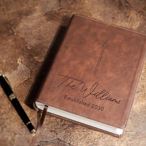 Personalized wedding Bible guestbook shown on ceremony table with flowers and rings. Custom engraved leather NIV Bible for religious wedding, Christian bridal shower gift, family Bible heirloom decor.