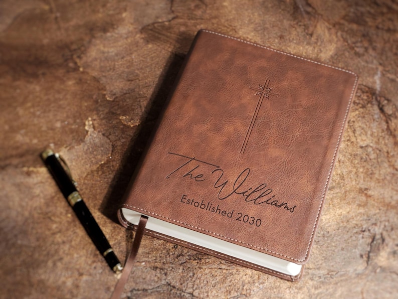 Personalized wedding Bible guestbook shown on ceremony table with flowers and rings. Custom engraved leather NIV Bible for religious wedding, Christian bridal shower gift, family Bible heirloom decor.