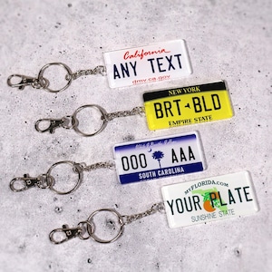 Car lover’s license plate keychain printed with your personalized message. Choose any state design for a fun and unique gift. Made from high-quality acrylic and attached to a sturdy metal keyring. Perfect for car enthusiasts, road-trip fans, and new drivers. A creative small gift that combines style and practicality for everyday keychain use.