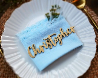 May include: A light blue napkin with a wooden place card that says "Christopher" on a white plate.