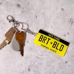 Personalized license tag keychain printed on premium acrylic with realistic state plate design. A great gift for car lovers, new drivers, and collectors. Choose any text, number, or location to create your own mini license plate keychain. A fun car key accessory that makes everyday driving more personal — perfect for birthdays, graduations, or stocking stuffers.
