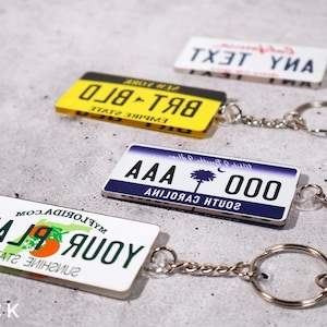 Car key accessory shaped like a custom license tag, made from crystal-clear acrylic with printed plate design. Personalized with any name, word, or number for a stylish and fun touch. A perfect driver’s gift, car lover’s keepsake, or travel souvenir. Ideal for both men and women who love cars, driving, or unique custom accessories that reflect their personality.