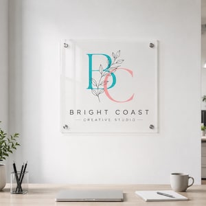 Custom painted acrylic business plaque with a colorful logo and black mounts displayed on a dark brick building facade.