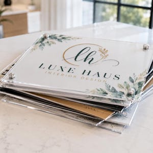 Stack of custom square acrylic logo plaques showing clear, white, black, and gold background options for business branding.