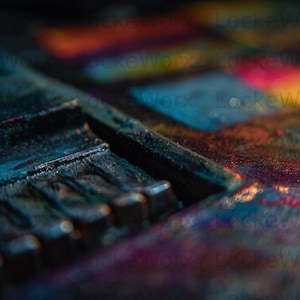 May include: Close-up of a paint palette with a variety of colors. The palette is dark with visible brushstrokes and textures. The colors include blue, orange, yellow, and pink, creating a vibrant and artistic display.
