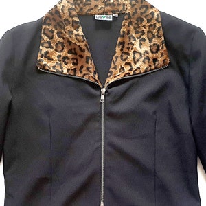 May include: A black jacket with a leopard print collar and cuffs. The jacket has a zipper closure and long sleeves. The leopard print features brown and tan spots on a tan background.