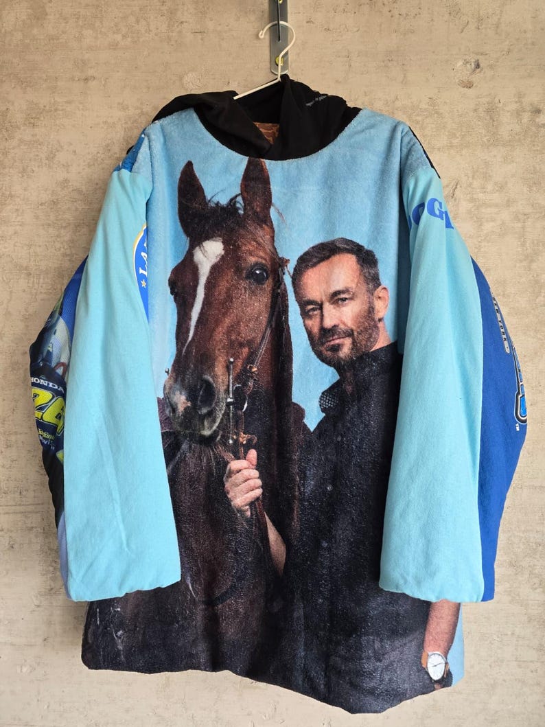 Pu&ograve; includere: Una felpa con cappuccio a maniche lunghe caratterizzata da una grande stampa fotografica di un cavallo marrone e una persona barbuta sul davanti. Il capo presenta maniche azzurre, un cappuccio nero e pannelli laterali blu.