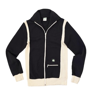 Könnte beinhalten: Schwarze Trainingsjacke mit cremefarbenen Seitenteilen und Bündchen. Die Jacke hat einen weißen Reißverschluss und ein kleines gesticktes Design auf der Brust. Der Kragen ist breit und zum Umklappen.