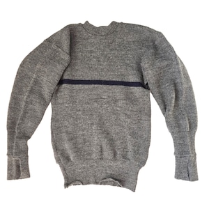 May include: A grey sweater with a dark blue horizontal stripe across the chest. The sweater has long sleeves with ribbed cuffs and a ribbed hem. The material appears to be a thick knit.