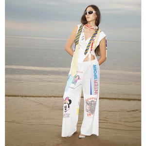 Può includere: Una persona indossa un top senza maniche bianco e pantaloni bianchi con varie toppe, tra cui una grafica di Minnie Mouse e la scritta "INTER SPORT". La persona indossa anche occhiali da sole e una sciarpa fantasia.