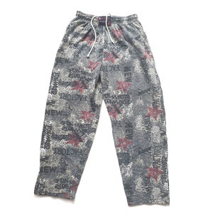 Könnte beinhalten: Graue Jogginghose mit weißem Kordelzug und Allover-Print. Der Druck enthält die Wörter "NEW" und "FACTORY" sowie Stern- und Blumendesigns in Rot und Weiß. Die Hose ist aus einem weichen Material.