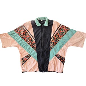May include: A vintage zip-up jacket with a unique color block design. The jacket features a black center panel, coral pink and teal accents, and floral patterned panels. The collar is a soft green.