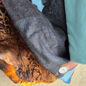 Pu&ograve; includere: Un articolo tessile multistrato caratterizzato da un prominente motivo leopardato con un volto felino dettagliato, una sezione testurizzata grigio antracite scuro e un pannello in tinta unita azzurro. Il tessuto mostra un mix di stampa animalier.