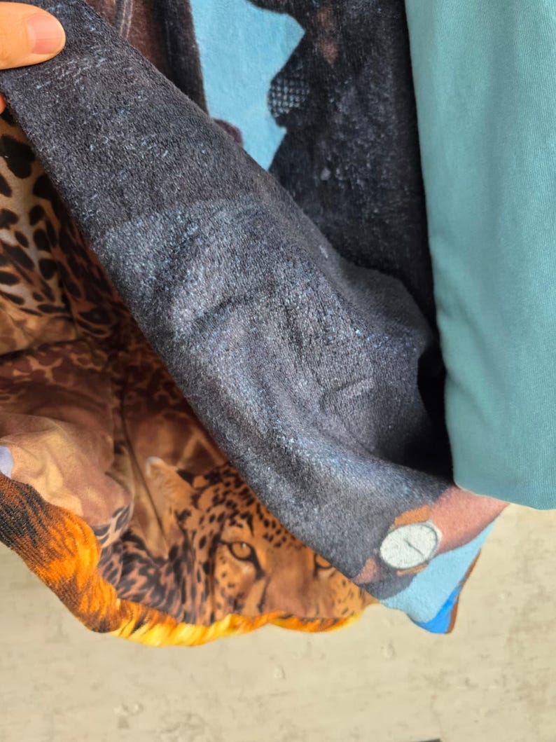 Pu&ograve; includere: Un articolo tessile multistrato caratterizzato da un prominente motivo leopardato con un volto felino dettagliato, una sezione testurizzata grigio antracite scuro e un pannello in tinta unita azzurro. Il tessuto mostra un mix di stampa animalier.