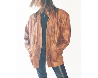 May include: A brown leather jacket with a button-up front and two pockets. The jacket has a classic design and a slightly worn appearance. The jacket is worn over a black top and dark blue pants.
