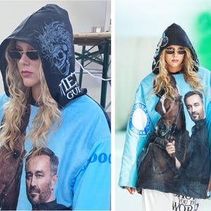 Pu&ograve; includere: Una felpa con cappuccio azzurra caratterizzata da una grande stampa fotografica di un uomo e un cavallo sul davanti. Il cappuccio nero mostra una grafica di un teschio con piume e il testo "MET GUIL". Le maniche sono azzurre con loghi circolari.
