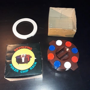 May include: A revolving poker chip rack set with a brown plastic chip holder, a white plastic ring, a cardboard box, and a box with the words "REVOLVING POKER CHIP RACK". The chip holder has red, white, and blue chips.