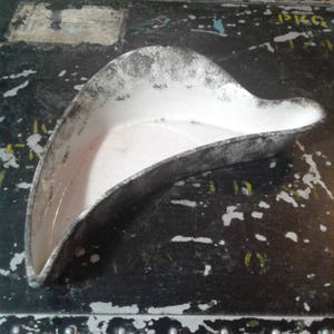 May include: A vintage, white ceramic dish with a unique, curved shape. The dish has a distressed, silver-colored rim and a smooth, white interior. The dish's design is reminiscent of a shallow, elongated bowl, perfect for serving or display.